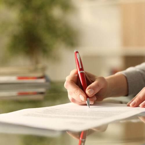 Close up of woman hands signing document with pen on a desk at home